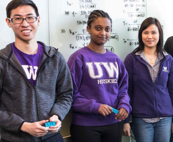 Group of engineering students standing with white board with formulas in the background 