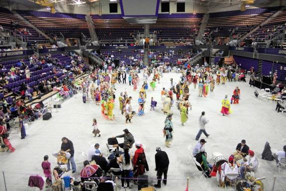 Overhead view of arena floor with dancers in regalia and other attendees gatheringgathered 