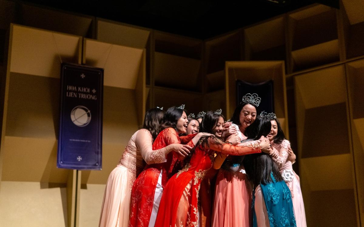 12 contestants of the pageant all hugging to celebrate their running mate for winning.  