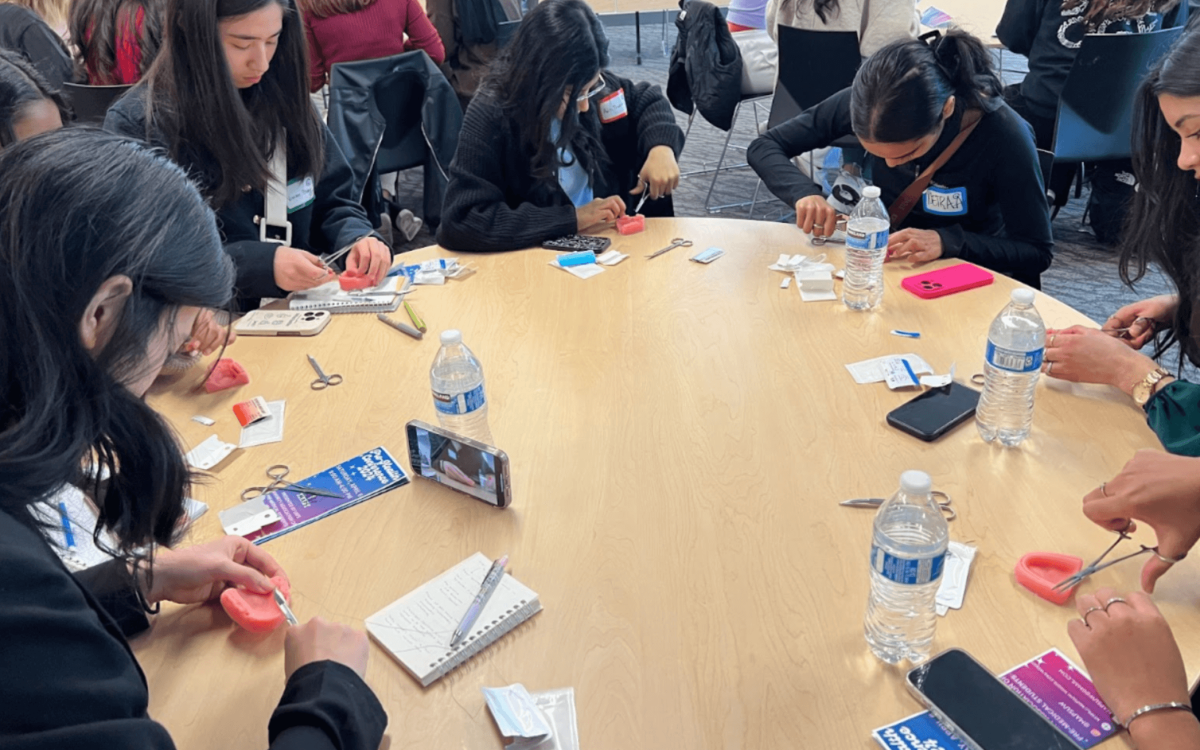 Suture Practice Workshop: A group of students sitting around a table practicing suturing techniques using simulated tools and silicone models.