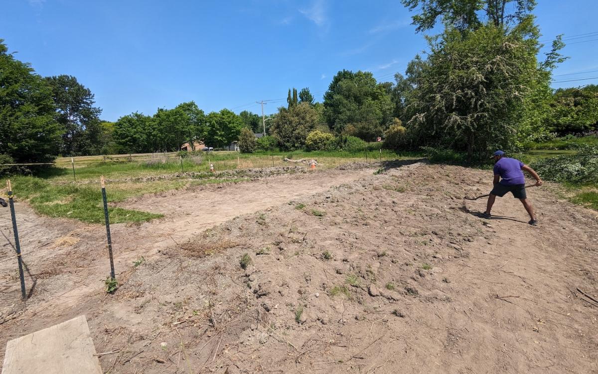 Person working the ground of the Wapato Pond, blue skies, trees in the background 