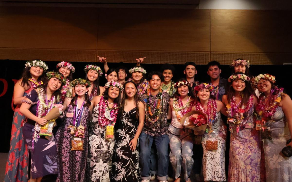 A group of students adorned in lei takes a group photo on the HUB ballroom stage.