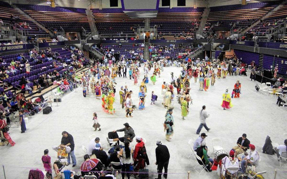 Overhead view of arena floor with dancers in regalia and other attendees gatheringgathered 
