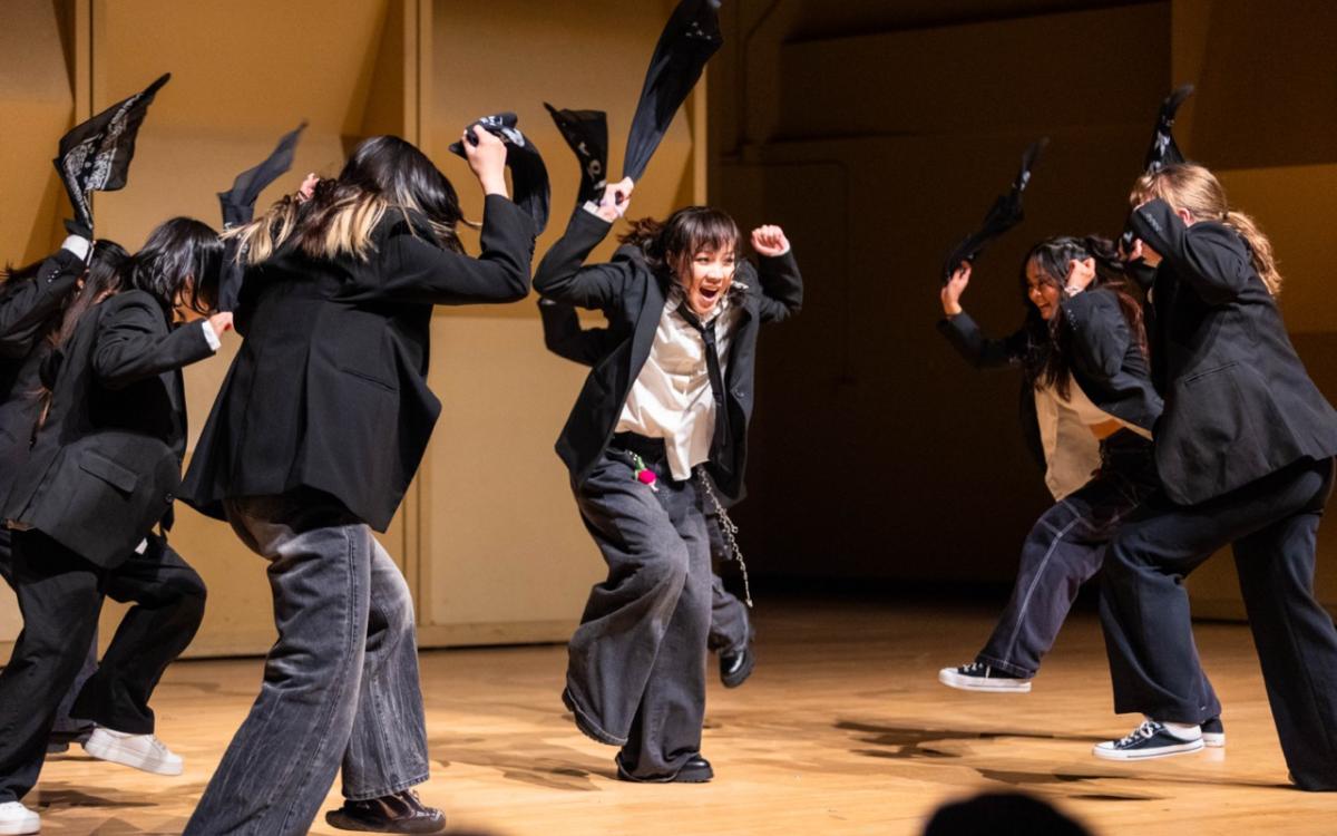 Group of dancers in black and white suit-style outfits dancing with bandanas.