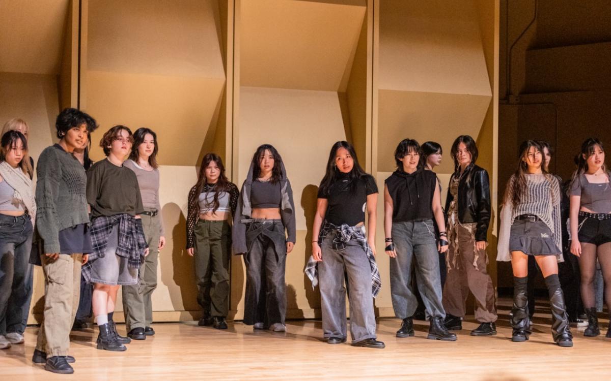 Group of dancers posing standing in grey outfits.